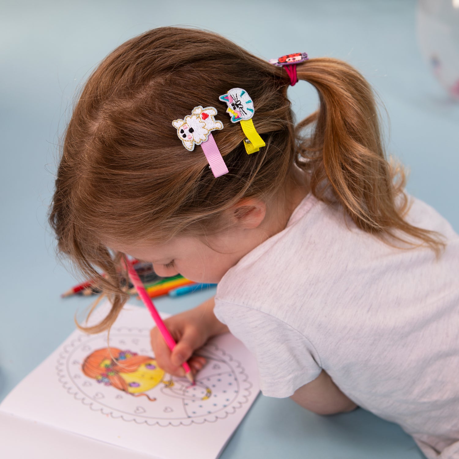 Rachel Ellen Designs hair accessories: a child is drawing in a colouring book, wearing colourful cat and dog embroidered hair clips.