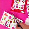 Temporary tattoos with gold foil being cut with scissors on a pink background