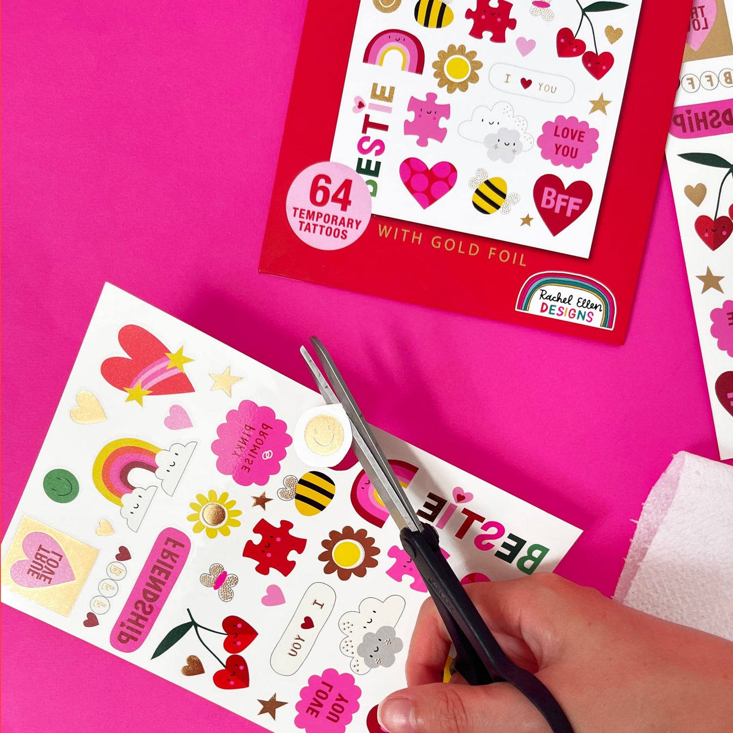 Temporary tattoos with gold foil being cut with scissors on a pink background