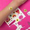 Colorful temporary tattoos on a pink background with a hand wearing a tattoo.