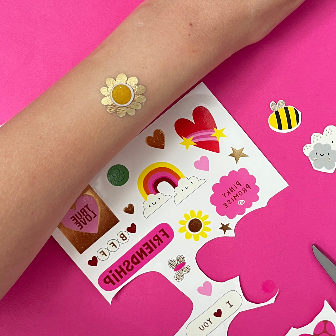 Colorful temporary tattoos on a pink background with a hand wearing a tattoo.