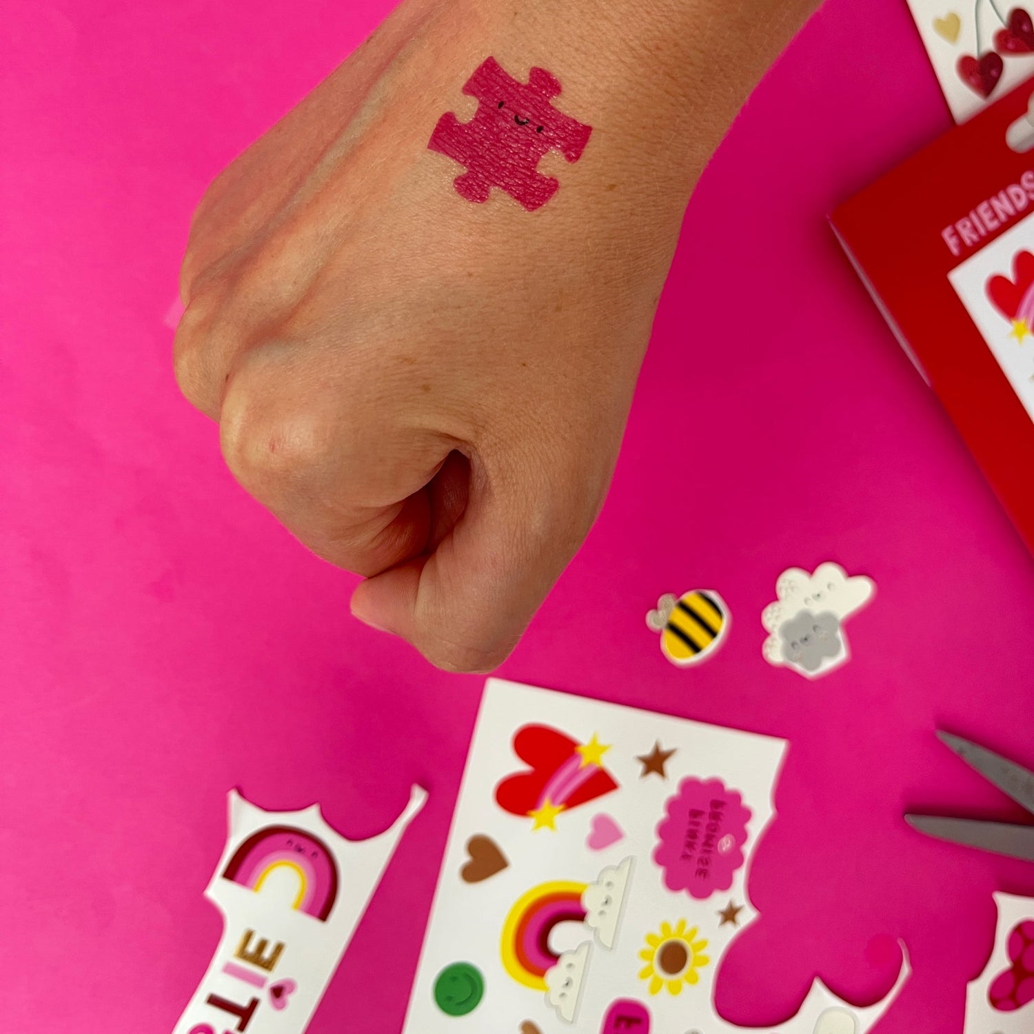 Hand with a temporary tattoo on a pink background with stickers and scissors.
