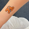 Temporary tattoo of a small dog on a person's arm with a white shirt in the background.